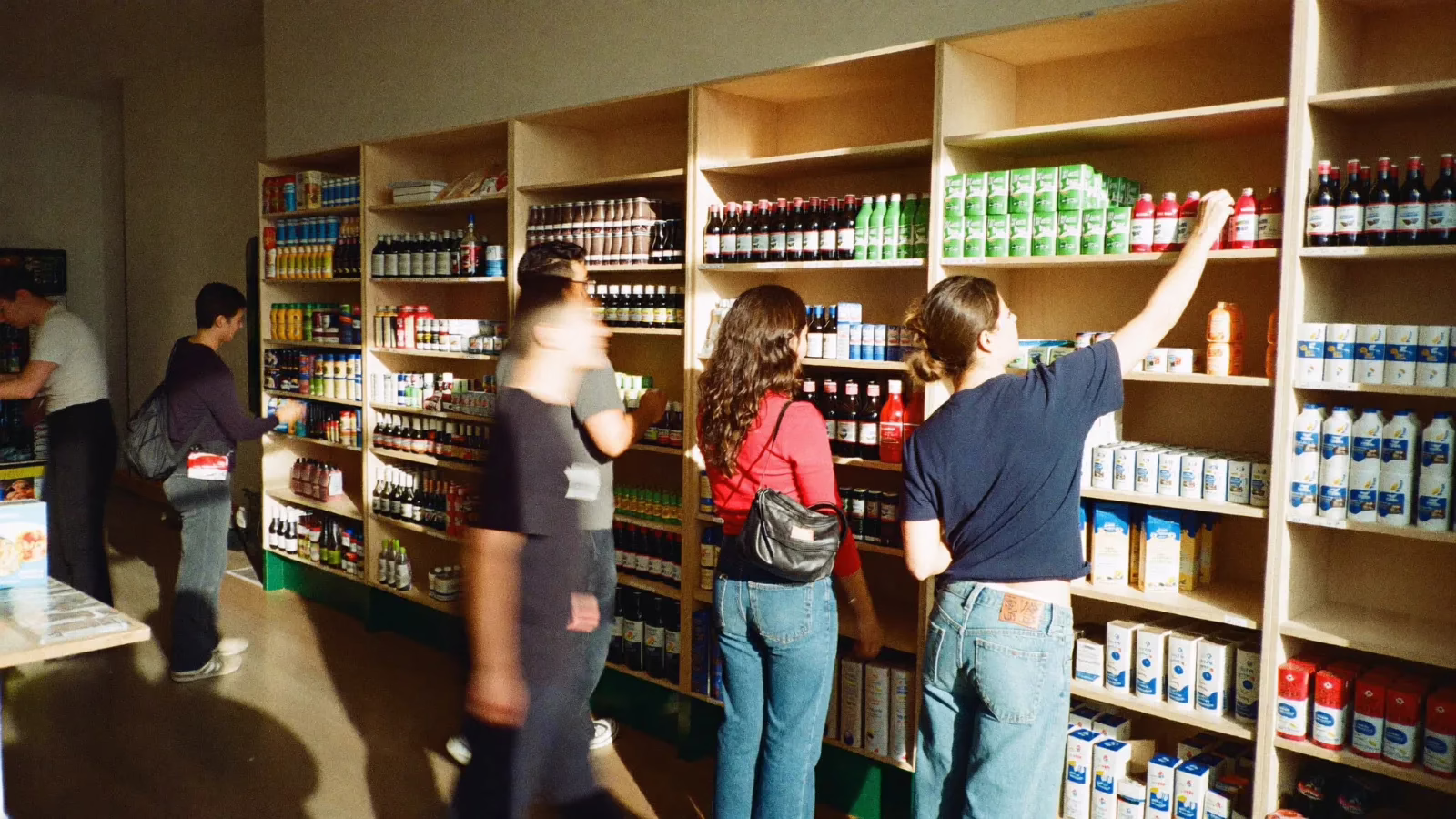 Kunder som tittar bland fulla hyllor i en butik medan en anställd fyller på en hylla