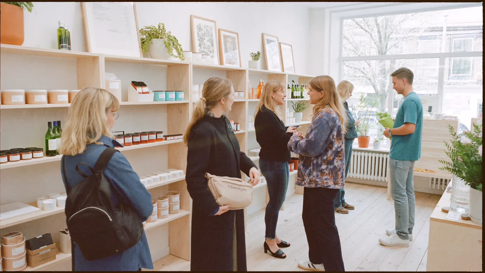 Ljus butik där kunder med olika bakgrund samtalar med ett butiksbiträde mellan hyllorna