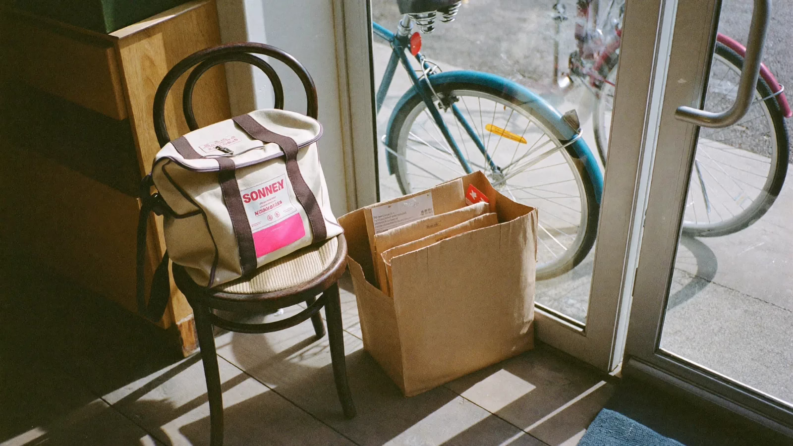 Kurirväska på en stol intill en kartong vid butiksdörren med en cykel utanför glaset