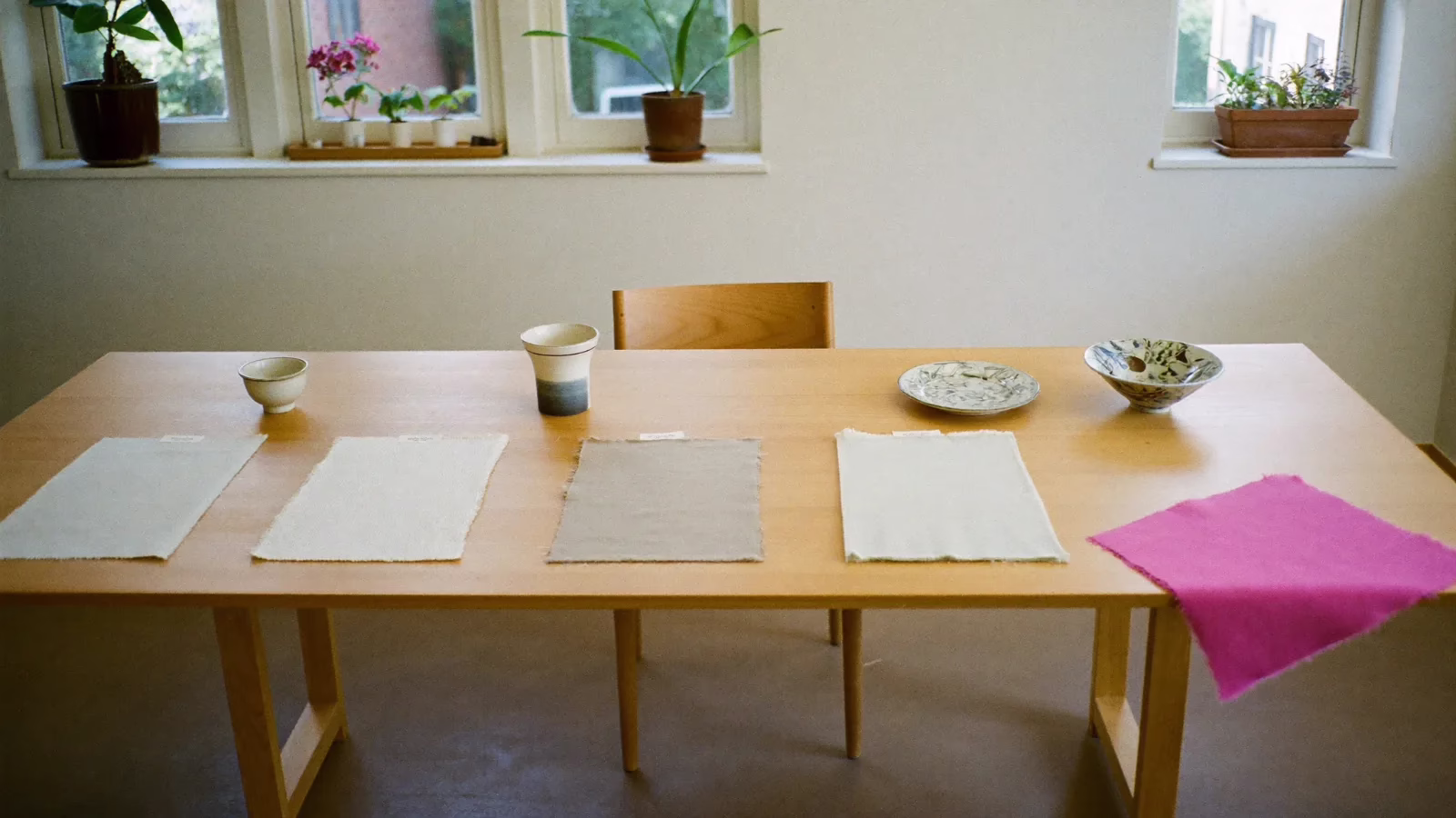 Långt träbord med fyra pappersark och några keramikskålar utlagda i rad