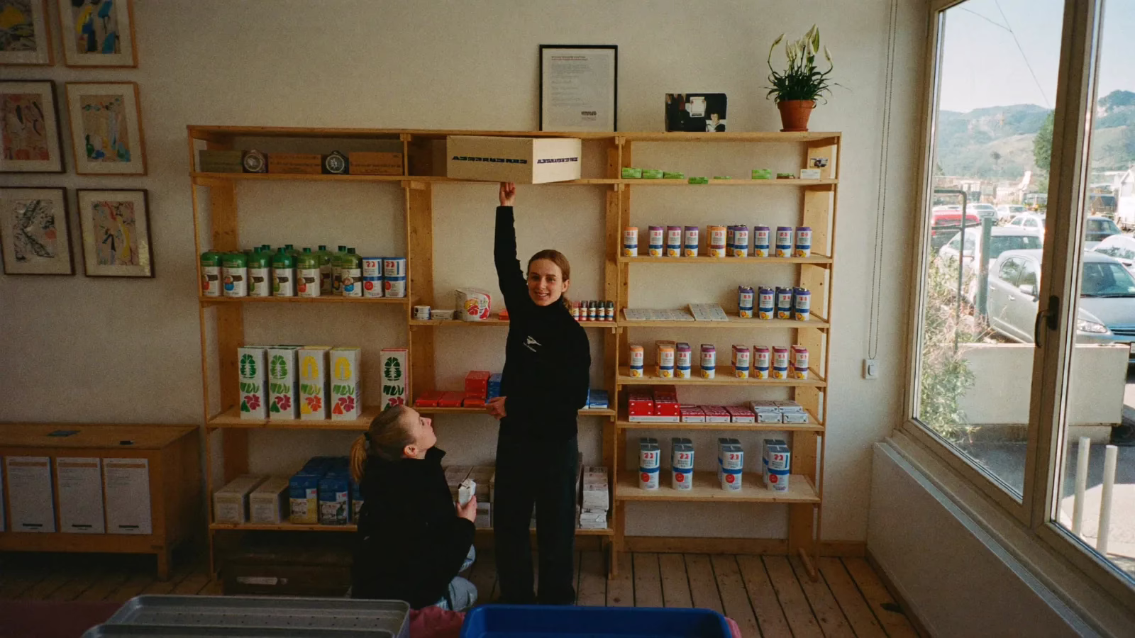 Butiksinnehavare sträcker sig upp mot en hög hylla medan en kund tittar upp och samtalar