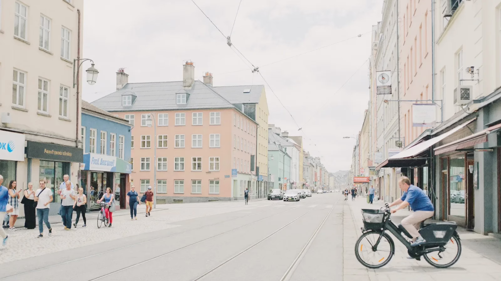 Ljus nordisk stadsgata med pastellfasader där människor går och cyklar förbi butikerna
