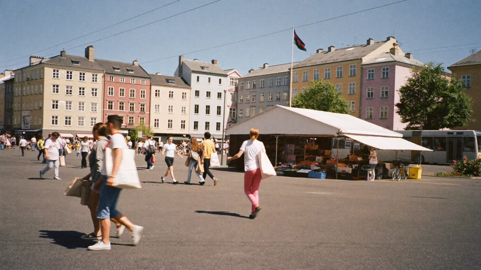 Nordiskt torg mitt på dagen med ett marknadsstånd och människor som handlar i solljus