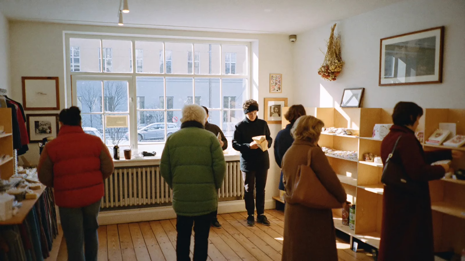 Kunder i vinterkappor tittar bland hyllorna i en butik med snö utanför fönstret