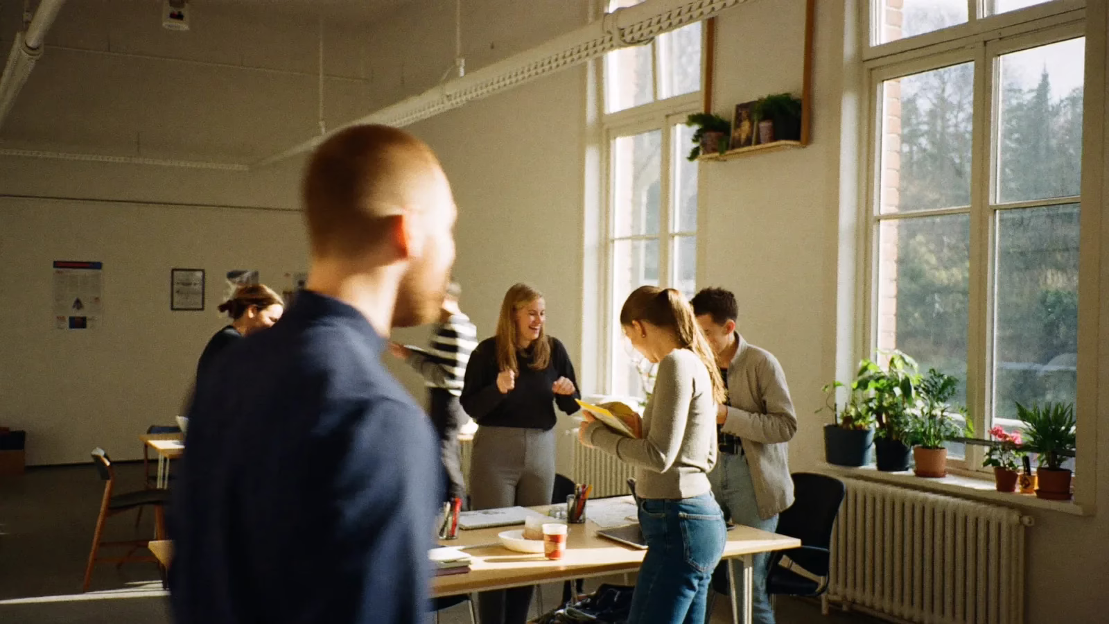 Ljus byråstudio där flera kollegor arbetar och samtalar vid ett långt bord i solljus